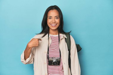 Kameralı ve sırt çantalı Filipinli kadın, mavi kişinin üstünde, bir tişört fotokopi alanını işaret ediyor, gururlu ve kendinden emin.