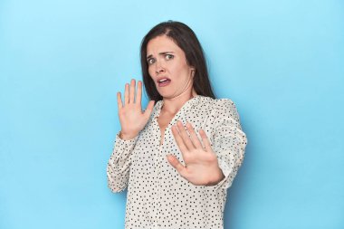 Mavi zemin üzerinde genç beyaz bir kadın yaklaşan tehlike nedeniyle şoka uğruyor.