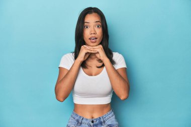 Mavi stüdyodaki Filipinli genç kadın şans için dua ediyor, şaşırıyor ve ağzını açıyor..