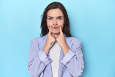 Mavi ceketli kadın mavi arka planda iki seçenek arasında şüphe ediyor..