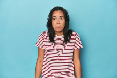 Mavi stüdyodaki Filipinli genç kadın omuzlarını silker ve gözleri açık kalır..