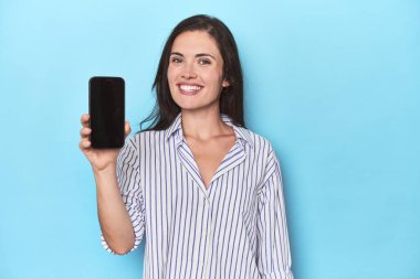 Mavi arkaplanda telefon ekranı gösteren kadın