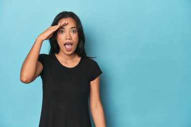 Mavi stüdyodaki Filipinli genç kadın yüksek sesle bağırıyor, gözleri açık ve elleri gergin tutuyor.