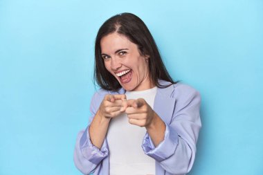 Mavi arka planda mavi ceketli kadın parmaklarıyla öne bakıyor..