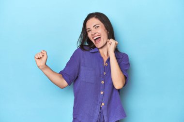 Genç beyaz kadın mavi arka planda dans ediyor ve eğleniyor..