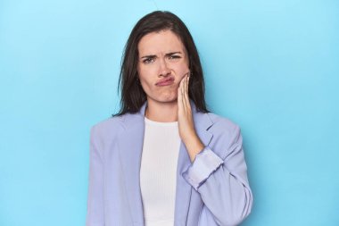 Mavi ceketli kadın mavi arka planda güçlü bir diş ağrısı ve azı dişi ağrısı var..