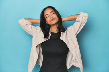 Mavi stüdyodaki Filipinli genç kadın elleri başının arkasında kendinden emin hissediyor..