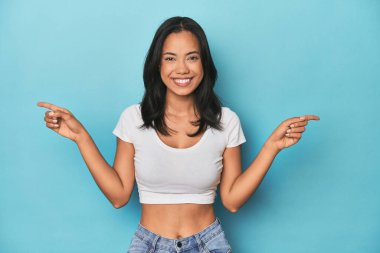 Mavi stüdyodaki Filipinli genç kadın farklı kopya alanlarını gösteriyor, birini seçiyor, parmaklarıyla gösteriyor.