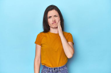 Mavi arka planda genç beyaz kadın güçlü bir diş ağrısı, azıdişi ağrısı var..