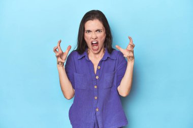 Mavi arka planda genç beyaz kadın öfkeyle çığlık atıyor..