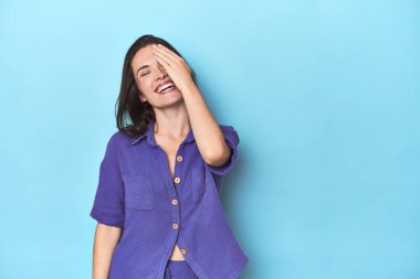 Mavi arka planda gülen, gülen, kaygısız, doğal duyguları olan beyaz bir kadın..