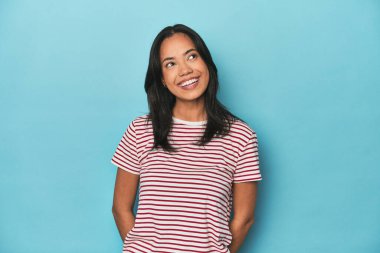 Mavi stüdyodaki Filipinli genç kadın gevşemiş ve mutlu bir şekilde gülüyor, boynunu uzatmış dişlerini gösteriyor..