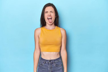 Mavi arka planda genç beyaz kadın komik ve dost canlısı bir dil uzatıyor..