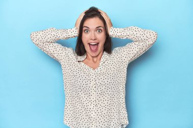 Mavi arka planda genç beyaz bir kadın çığlık atıyor, çok heyecanlı, tutkulu, bir şeyden memnun..