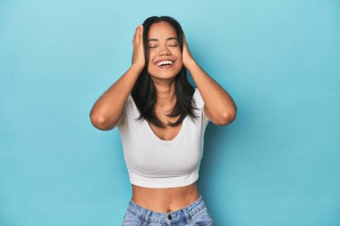 Mavi stüdyodaki Filipinli genç kadın ellerini başının üstünde tutarak neşeyle gülüyor. Mutluluk kavramı.