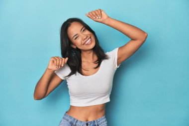 Mavi stüdyodaki Filipinli genç kadın özel bir günü kutluyor, atlıyor ve enerji ile kollarını kaldırıyor..