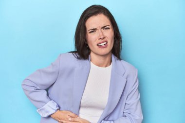 Mavi ceketli kadın mavi arka planda, karaciğer ağrısı ve karın ağrısı var..