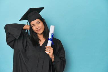Mavi stüdyodaki diplomasıyla Filipinli mezun kafasının arkasına dokunuyor, düşünüyor ve bir seçim yapıyor..