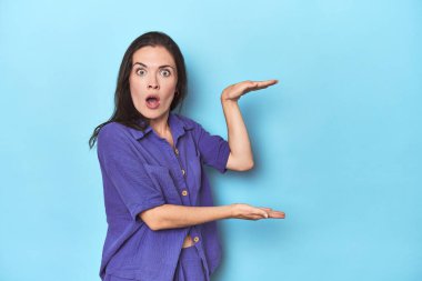 Mavi arka plandaki genç beyaz kadın elleri arasında bir fotokopi alanı tutarken şok ve şaşkınlık yaşadı..