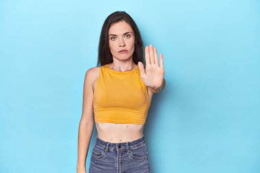Mavi arka planda duran genç beyaz kadın elini uzatmış, dur işareti göstererek seni engelliyor..