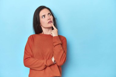 Mavi arka planda beyaz bir kadın şüpheli ve şüpheci bir ifadeyle yana bakıyor..