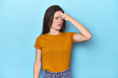 Kafkasyalı genç bir kadın mavi arka planda, başı ağrıyor, yüzüne dokunuyor..