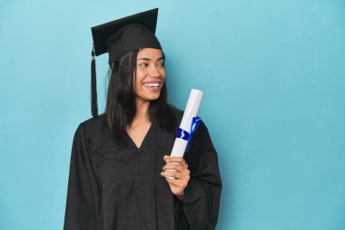 Mavi stüdyodaki diplomasıyla Filipinli mezun. Gülümsüyor, neşeli ve keyifli..