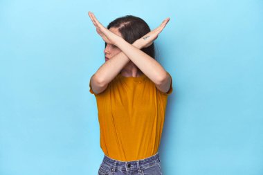 Mavi arka planda genç beyaz kadın iki kolu çapraz tutuyor, inkar kavramı.