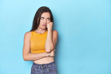 Mavi arka planda oturan, üzgün ve dalgın hisseden, fotokopi alanına bakan beyaz bir kadın..