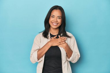 Mavi stüdyodaki Filipinli genç kadın avuçlarını göğsüne bastıran dostça bir ifadeye sahip. Aşk konsepti.