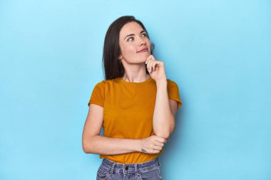 Kafkasyalı genç bir kadın mavi arka planda düşünür ve bakar, yansıtır, düşünür, hayal kurar..