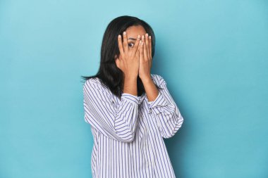 Mavi stüdyodaki Filipinli genç kadın korkmuş ve gergin parmaklarıyla göz kırpıyor..