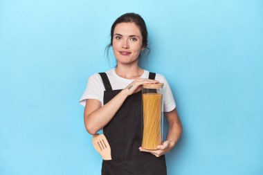 Genç aşçı mavi önlükle makarna kavanozu tutuyor