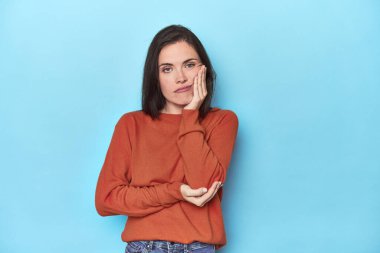 Mavi arka planda oturan, sıkılmış, yorgun ve dinlenmeye ihtiyacı olan beyaz bir kadın..