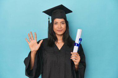 Mavi stüdyodaki diplomasıyla Filipinli. Gülümsüyor. Beş numarayı parmaklarıyla gösteriyor..