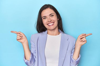 Mavi arka planda mavi ceketli kadın farklı kopya alanlarını gösteriyor, birini seçiyor, parmaklarıyla gösteriyor..