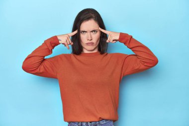 Mavi zemin üzerinde genç beyaz kadın bir göreve odaklanmış, parmaklarını işaret ediyor..