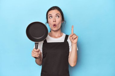 Mavi arka planda önlüğü ve tavası olan kadının harika bir fikri var, yaratıcılık kavramı..