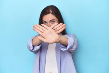 Mavi ceketli kadın, mavi arka planda inkar jesti yapıyor.