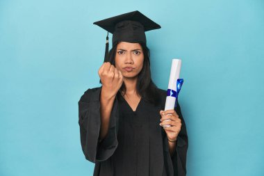 Mavi stüdyodaki diplomasıyla Filipinli. Kameraya yumruğunu gösteriyor. Yüzünde agresif bir ifade var..