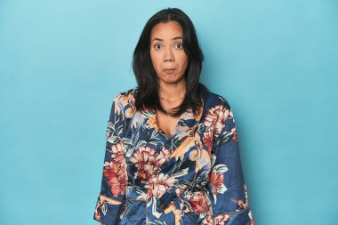 Çiçekli kimonolu Filipinliler mavi stüdyoda omuz silkiyor ve gözleri açık..