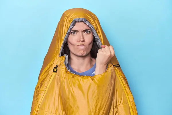 カメラに拳を示す青い背景の寝袋の女性 積極的な表情 — ストック写真
