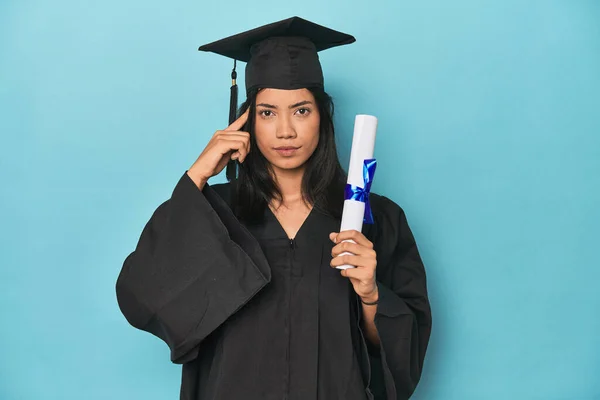 Filipina Graduate Diploma Blue Studio Pointing Temple Finger Thinking Focused — Stock Photo, Image