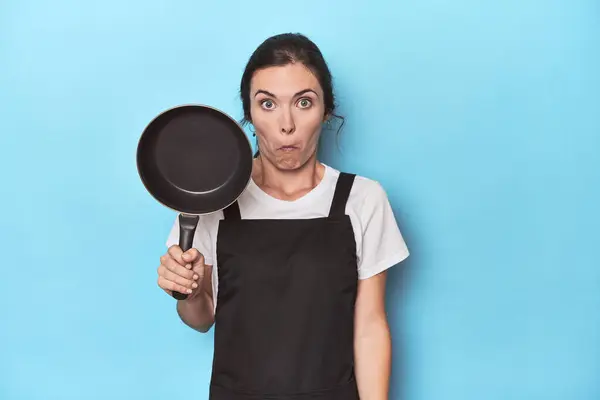 Woman Apron Pan Blue Background Shrugs Shoulders Open Eyes Confused — Stock Photo, Image