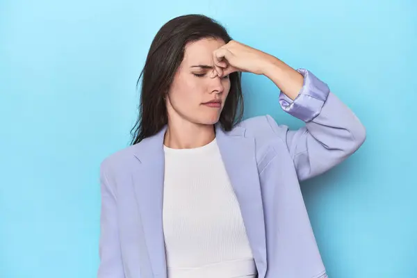 Mavi Ceketli Kadın Mavi Arka Planda Başı Ağrıyor Yüzüne Dokunuyor — Stok fotoğraf
