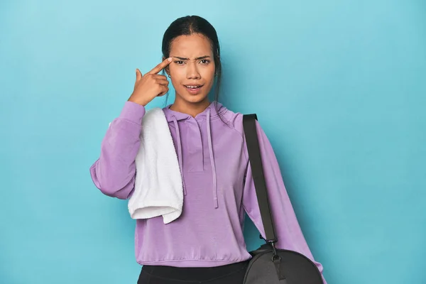 Filipina with gym gear on blue studio showing a disappointment gesture with forefinger.