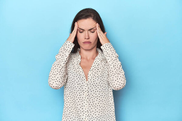 Young caucasian woman on blue backdrop touching temples and having headache.