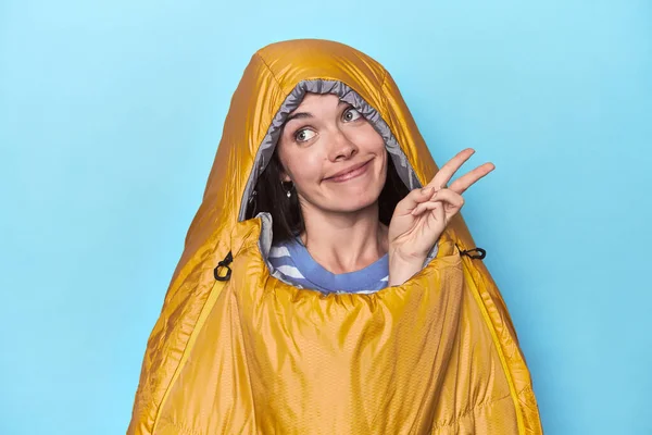 穿着蓝色背景睡袋的女人快乐而无忧无虑 用手指展示和平的象征 — 图库照片