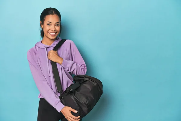 Young Filipina with sports backpack for the gym on blue backdrop