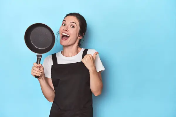 Woman Apron Pan Blue Background Points Thumb Finger Away Laughing — Stock Photo, Image